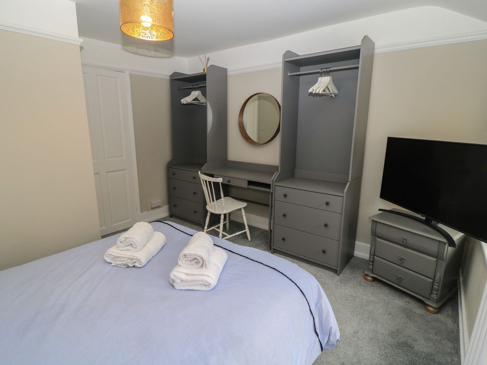 A bedroom with a bed, wardrobe, desk, and television at Still Waters in Swanage