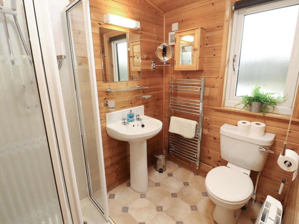 A bathroom with wooden walls featuring a shower, sink, toilet, and towel rail at The Fold, Number 28, Burnside Park near Keswick