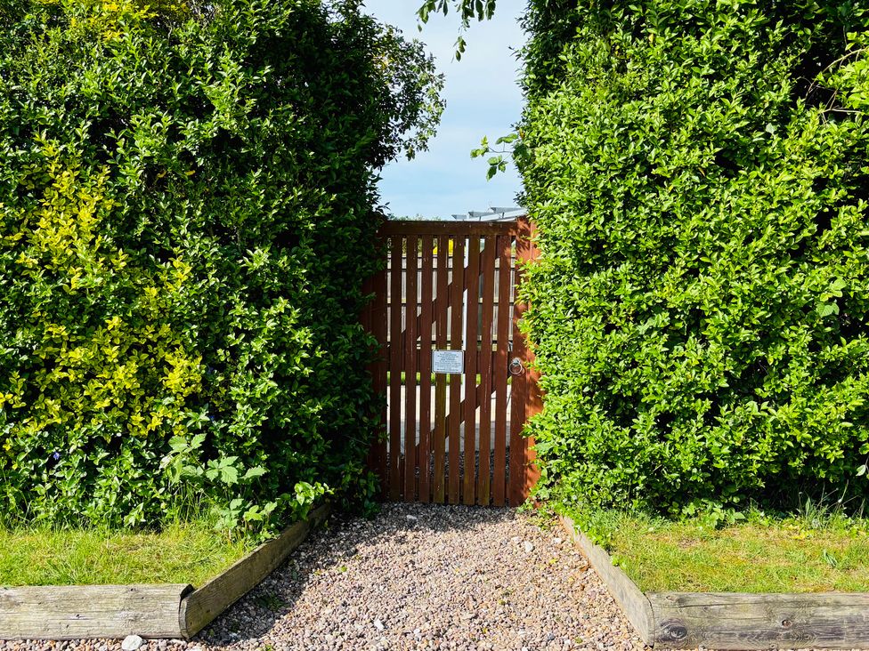 A gate surrounded by hedges leading to a gravel path at The Old Gate House Annexe in Alford