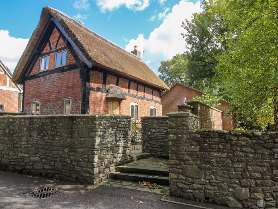 A thatched house with a stone wall and pathway at Manor Cottage in Little Stretton near Church Stretton
