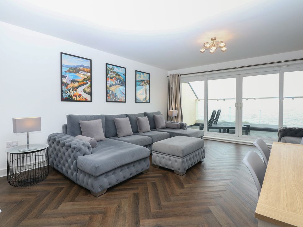 A living room with a gray sofa and artwork at 26 Awel Y Mor in Pwllheli