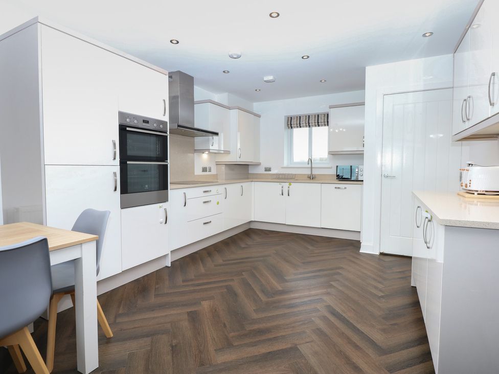 A kitchen with modern appliances and a dining table at 26 Awel Y Mor in Pwllheli