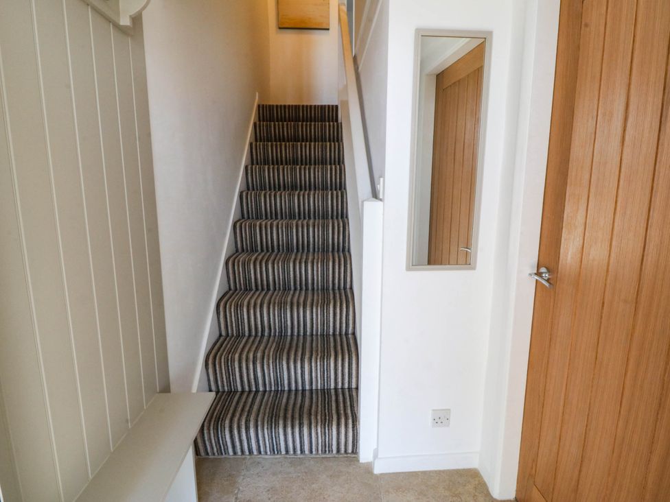 A hallway with stairs and a mirror at 4 Bryn Llan Aberdaron