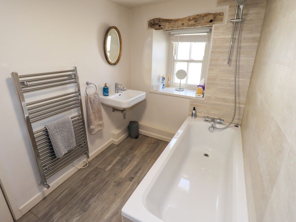 A bathroom with a bathtub, sink, and towel rack at Bridge End Cottage in Haverthwaite near Cartmel