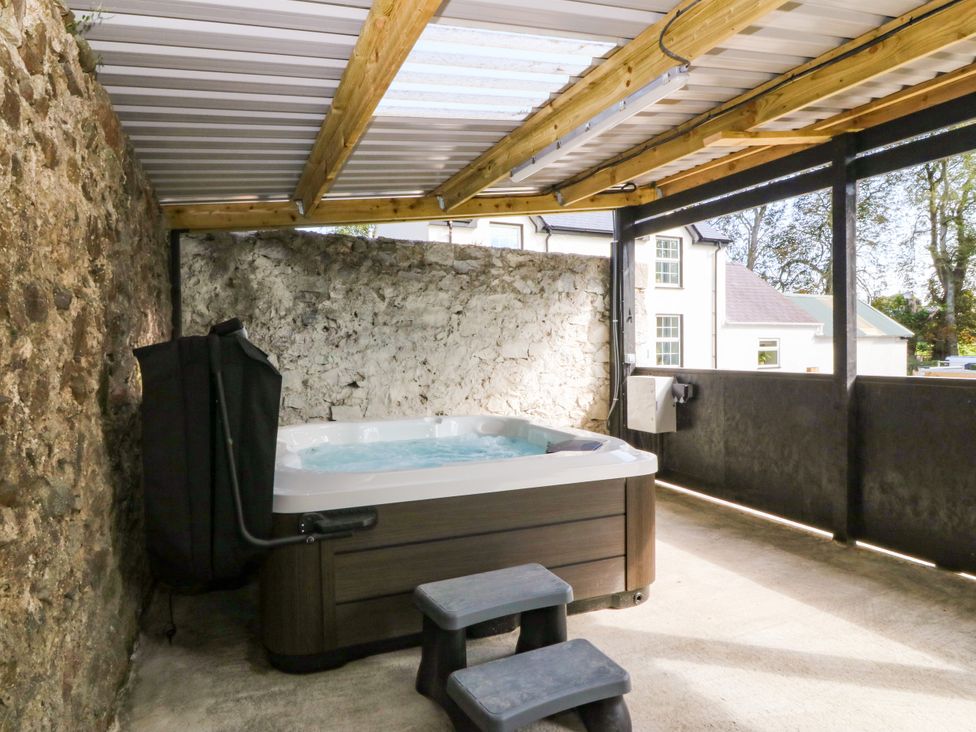 An outdoor area with a hot tub and stone wall at Gate House in Capel Coch near Llanerchymedd