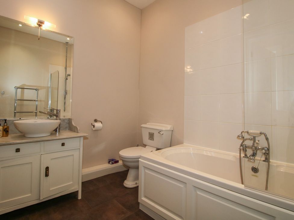 A bathroom with a bath tub, toilet, sink, and mirror at The Butler’s Quarters in Bourton near Much Wenlock
