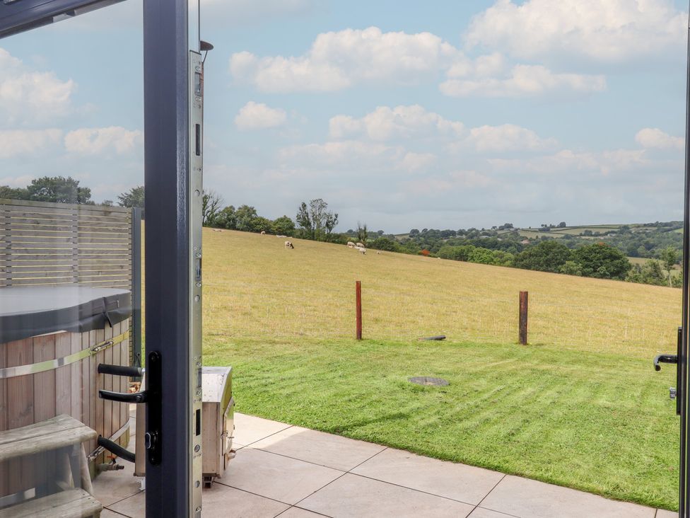 A view from an outdoor patio showing a field and hot tub at The Cadeleigh near Tiverton