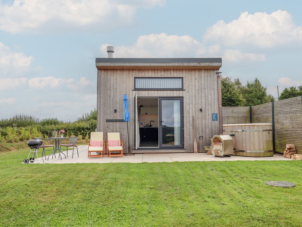 An outdoor area with a wooden building, table, chairs, barbecue and hot tub at The Cadeleigh in Cadeleigh near Tiverton