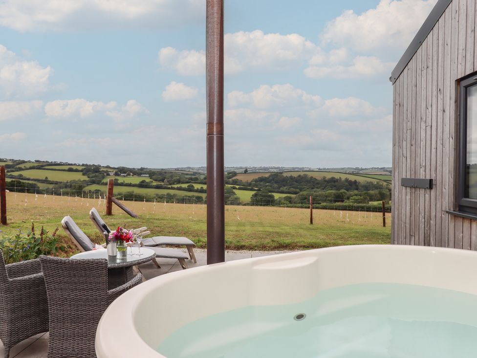 An outdoor area with a hot tub and chairs overlooking the countryside at The Pennymoor in Cadeleigh near Tiverton