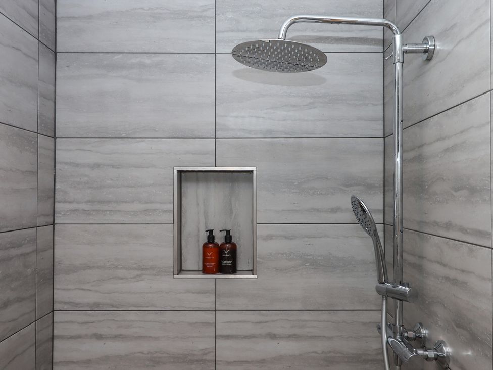 A shower area with a showerhead and products on a shelf at The Pennymoor in Cadeleigh near Tiverton