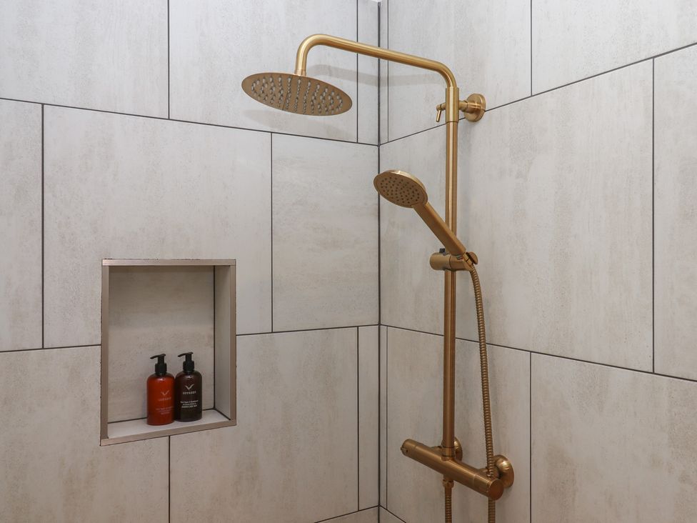 A shower with a gold shower head and niche containing shampoo and conditioner at The Bickleigh Cadeleigh near Tiverton