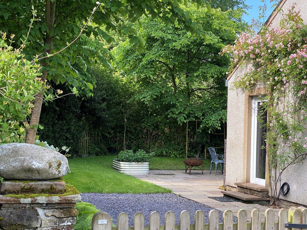 A garden with trees, rock, chair, and patio at Greywalls in Maulds Meaburn