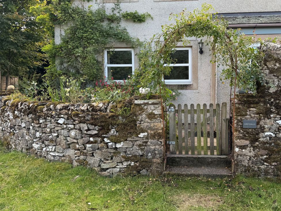 A stone wall with a wooden gate and flowerbed at Greywalls in Maulds Meaburn