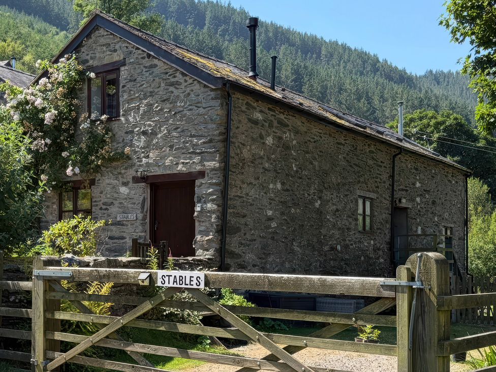 An outdoor view of a stone building with a gate and sign at Graig Las The Stables Llanrhaeadr-Ym-Mochnant