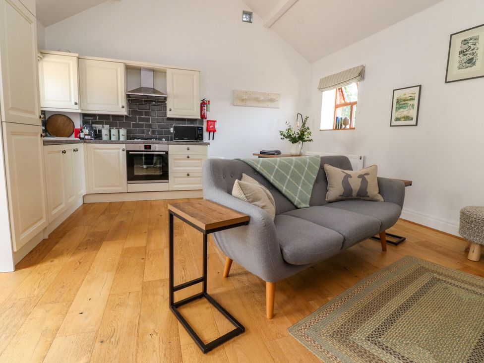 A living room with a sofa and kitchen area at The Stables in Hall Green near Walmer Bridge