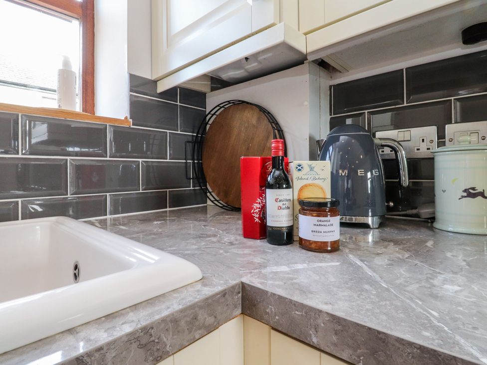 A kitchen countertop with a sink, wine bottle, marmalade jar, kettle, and cutting board at The Stables in Hall Green near Walmer Bridge