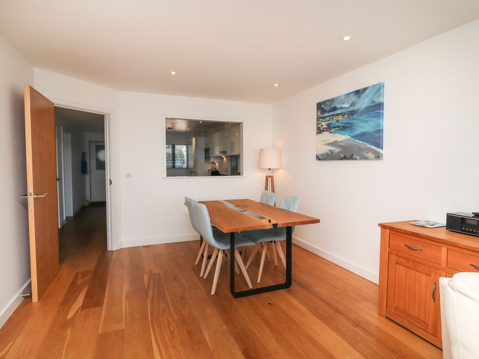 A dining area with a wooden table and four light blue chairs near a floor lamp and a wooden cabinet in a room with white walls and hardwood flooring at Kittiwake Carbis Bay