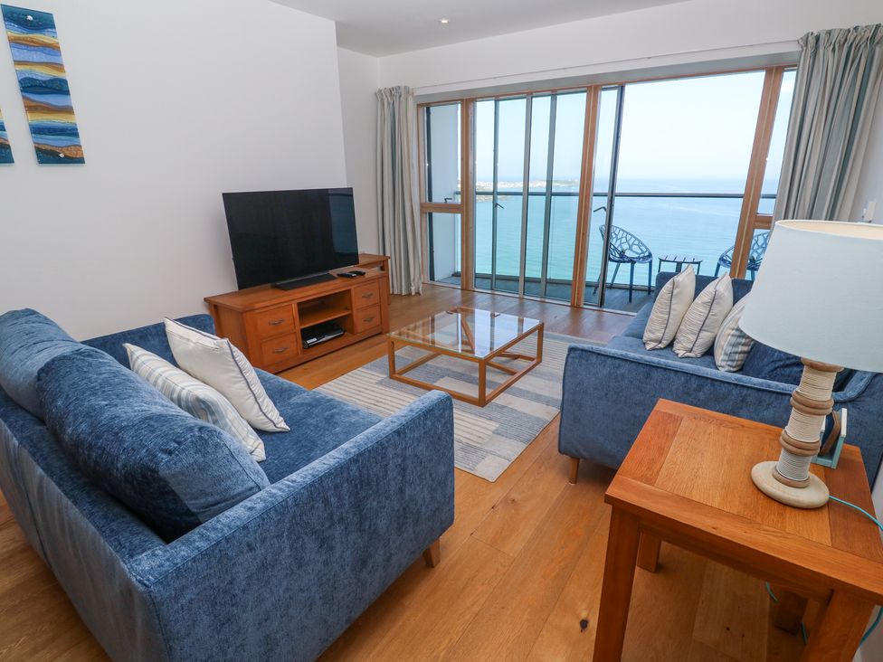 A living room with blue sofas a wooden coffee table a flat screen tv on a stand and a balcony overlooking the sea at Kittiwake in Carbis Bay