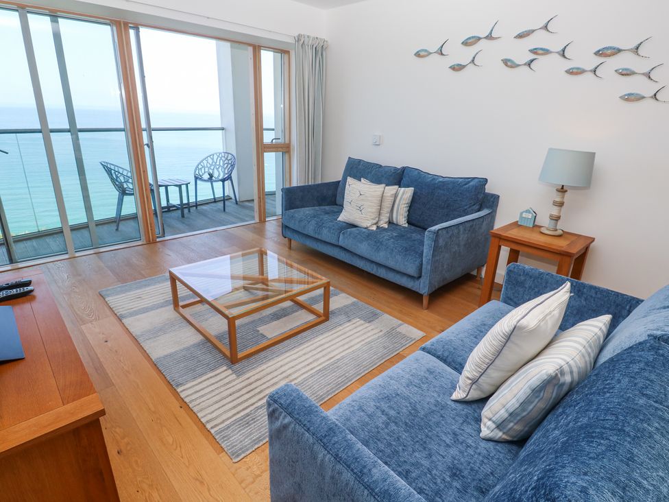 A living room with two blue sofas a glass coffee table and a balcony overlooking the sea at Kittiwake in Carbis Bay