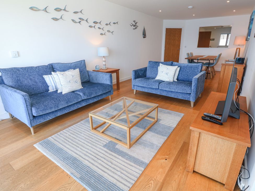 A living room with two blue sofas and a glass coffee table on a striped rug at Kittiwake in Carbis Bay