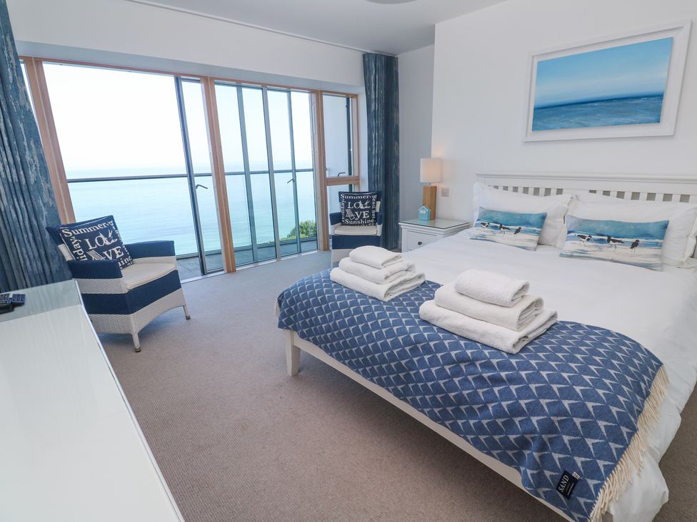 A bedroom with a double bed, two chairs, bedside tables, and large windows with ocean view at Kittiwake in Carbis Bay