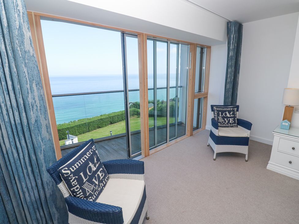 A room with two blue and white chairs facing a floor to ceiling glass door overlooking the sea at Kittiwake in Carbis Bay