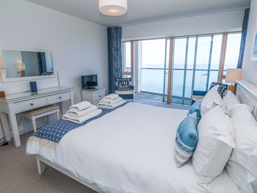 A bedroom with a bed facing large sliding glass doors overlooking the sea at Kittiwake in Carbis Bay