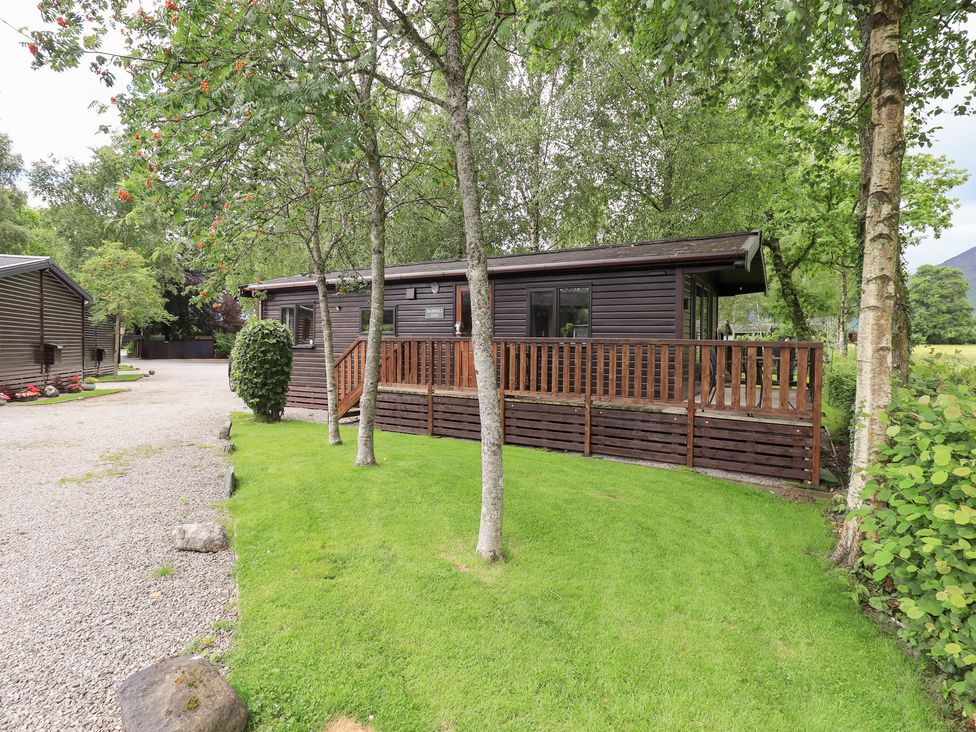 A cabin with a deck surrounded by grass and trees at Squirrels Leap, Number 29, Burnside Park near Keswick
