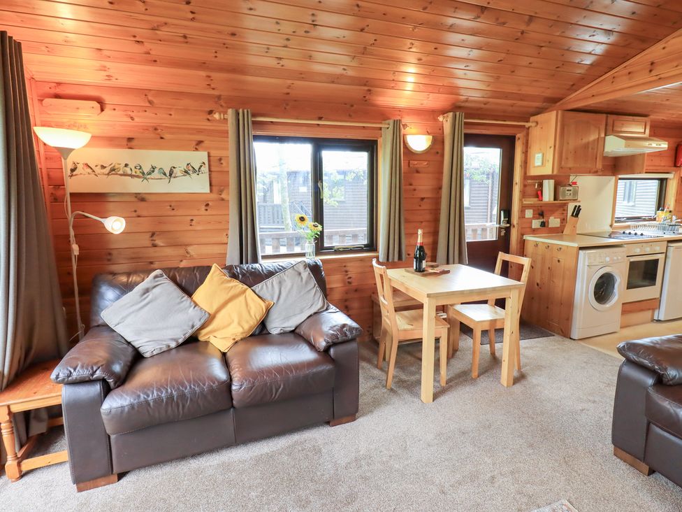 A living room with a sofa, dining table, and kitchen unit at Squirrels Leap, Number 29, Burnside Park near Keswick