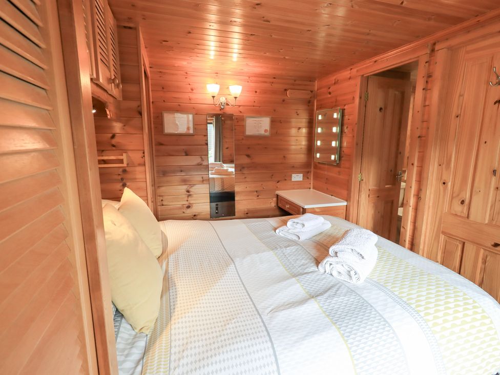 A bedroom with wooden walls and a bed with pillows and towels at Squirrels Leap, Number 29, Burnside Park near Keswick