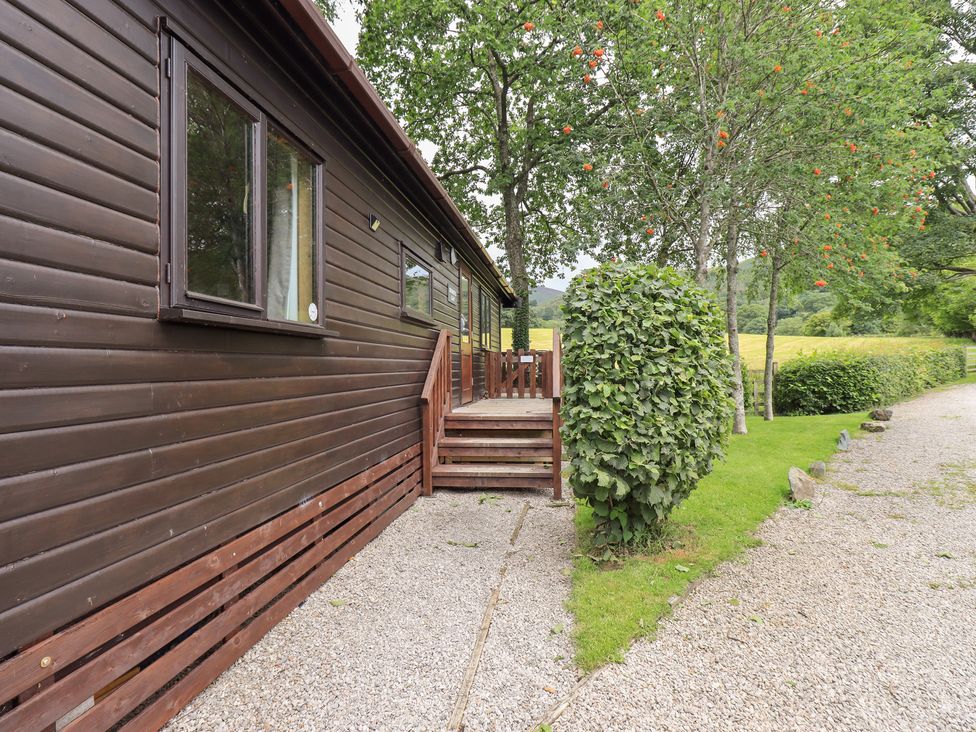 An outdoor view of a wooden cabin with steps and surrounding greenery at Squirrels Leap, Number 29, Burnside Park near Keswick