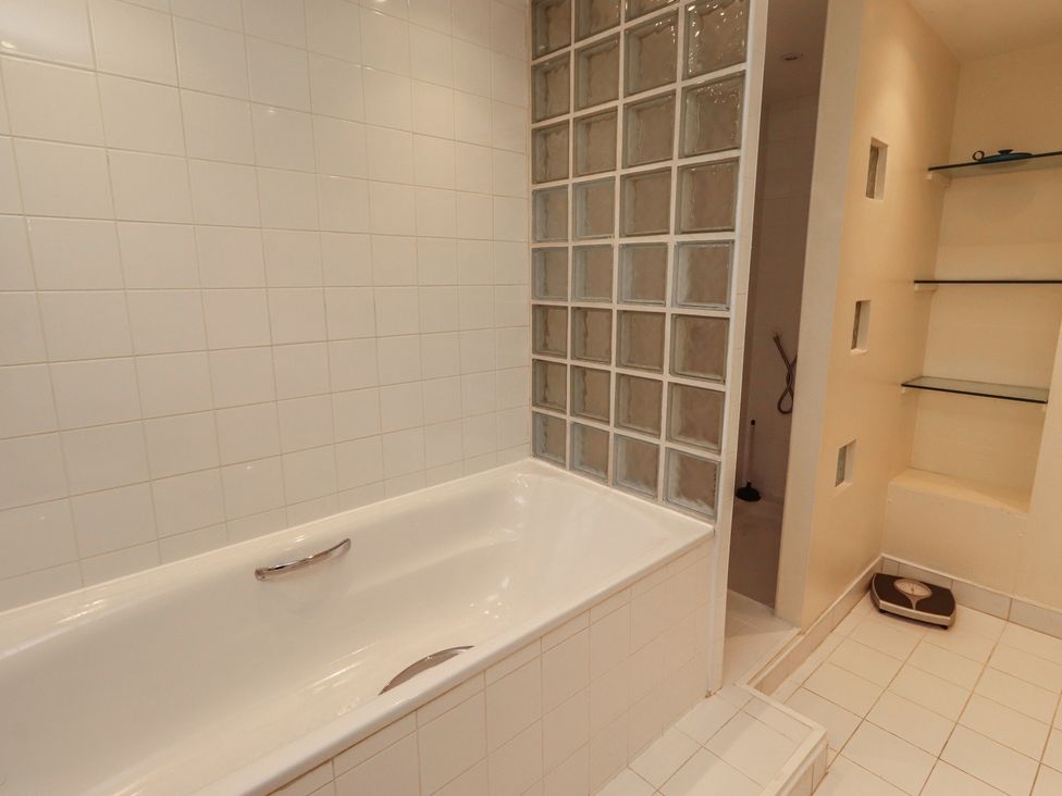 A bathroom with a bathtub and a glass block wall at ASTA COTTAGE in Cresswell