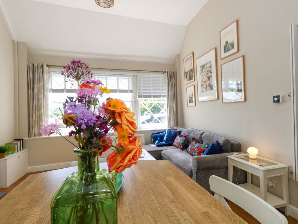 A living room with a dining table and flowers in a vase at Sea Pink Cottage in Langton Matravers
