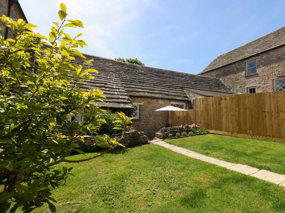 A garden with a stone building and a parasol at Sea Pink Cottage in Langton Matravers