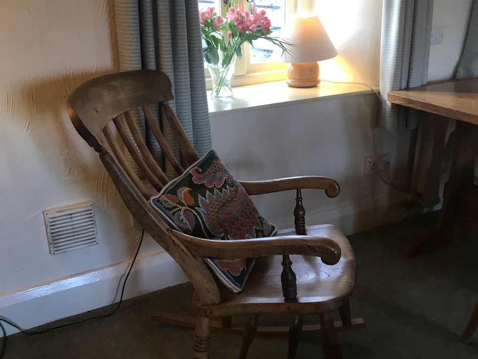 A living room with a rocking chair and flowers on the windowsill at Tyee Cottage in Burton-In-Kendal