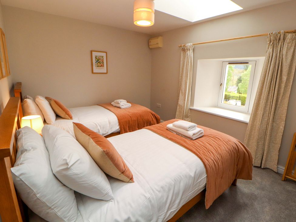 A bedroom with two beds, window, and bedside lamp at Swallow's Nest Thornthwaite near Braithwaite