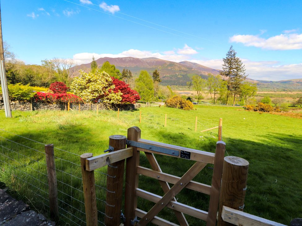 A view of a gate and green field with mountains in the background at Swallow's Nest in Thornthwaite near Braithwaite
