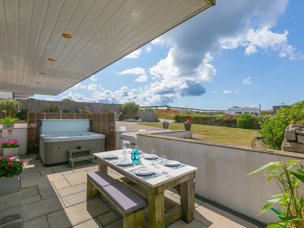 An outdoor area with a dining table and hot tub at Sandbanks in Praa Sands