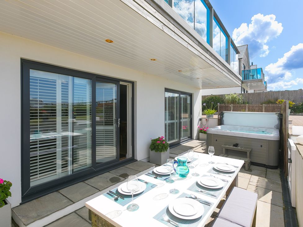 An outdoor patio with a hot tub and dining table at Sandbanks in Praa Sands