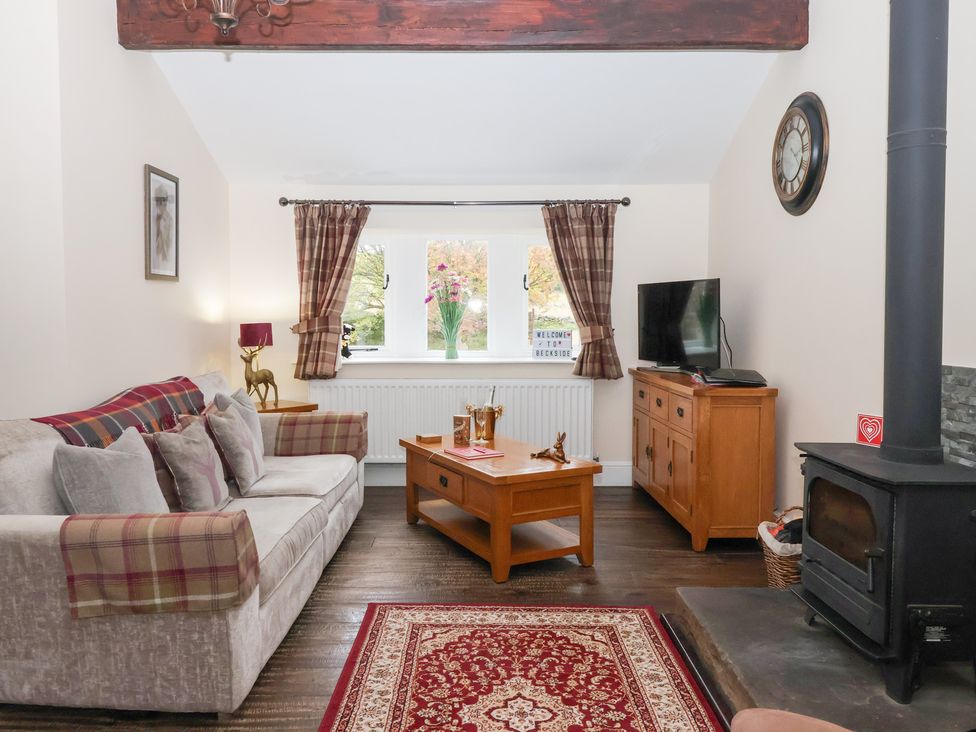 A living room with a sofa, table, and television at Beckside Cottage in Cowling near Skipton