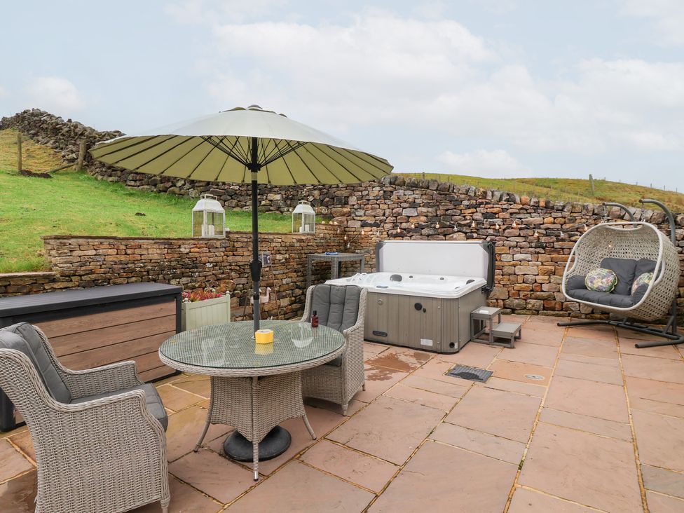 An outdoor seating area with a hot tub and patio furniture at Beckside Cottage in Cowling near Skipton