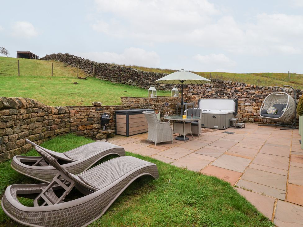 A garden with lounge chairs and a hot tub at Beckside Cottage Cowling near Skipton