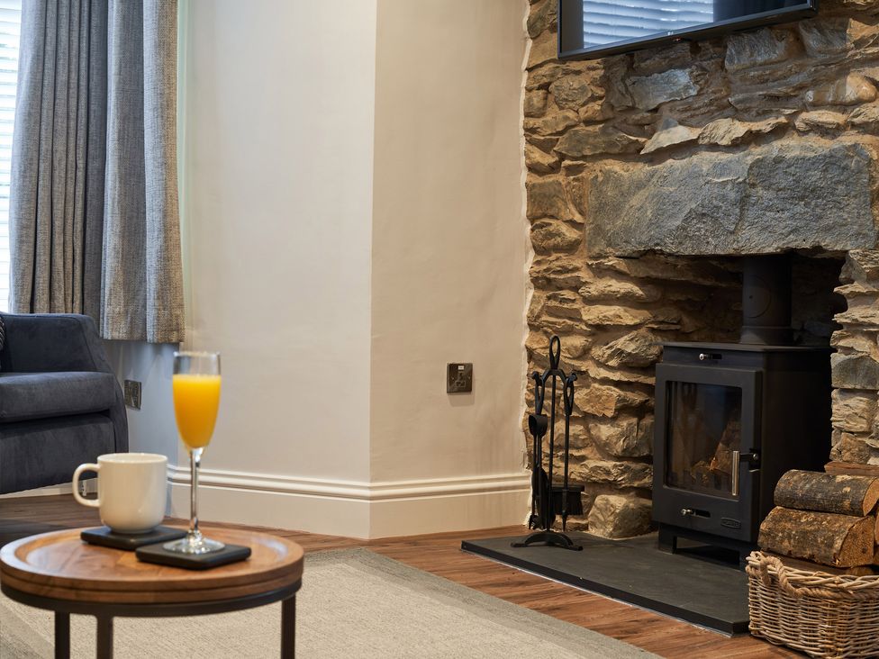 A living room with a stone fireplace wood burner a glass of orange juice and a mug on a table at Lower Sheriff's Place in Windermere