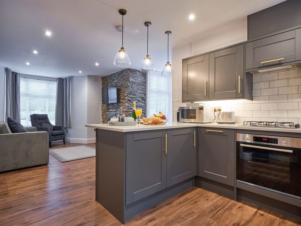 A kitchen with gray cabinets and an oven next to a living area with a gray sofa and armchair at Lower Sheriff's Place in Windermere