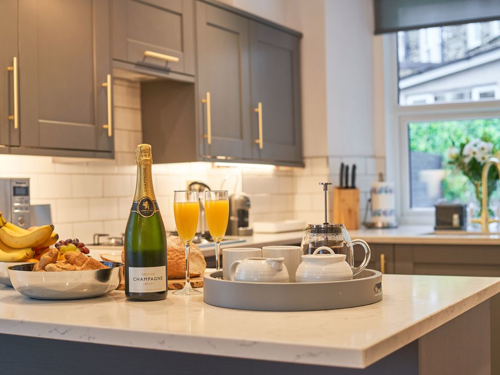 A kitchen countertop with a bottle of champagne two glasses of orange juice a bowl of fruit and pastries and a tray with cups at Lower Sheriff's Place in Windermere