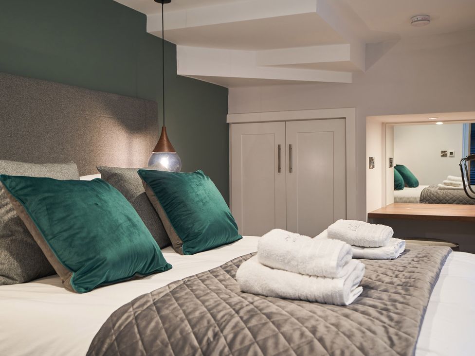 A bedroom with a bed with green and gray pillows folded towels on a quilted bedspread and a white cabinet at Lower Sheriff's Place in Windermere