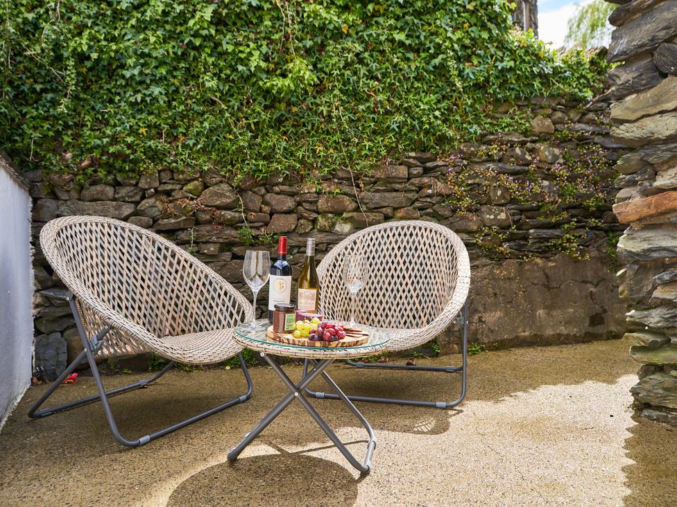 Two wicker chairs with a small round glass table holding two wine bottles grapes and jars against a stone wall with ivy at Lower Sheriff's Place in Windermere