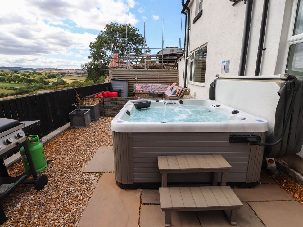 A hot tub on a patio with outdoor furniture at Tyddyn Elidir near Old Colwyn