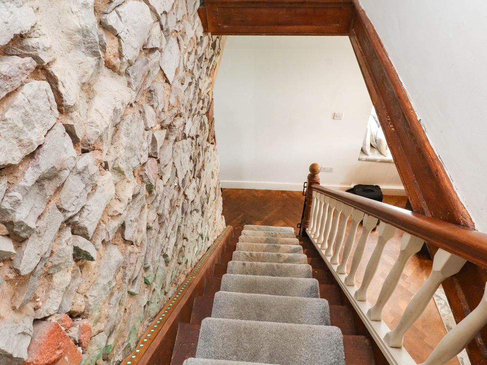 A staircase with a wooden handrail and stone wall at Tyddyn Elidir near Old Colwyn