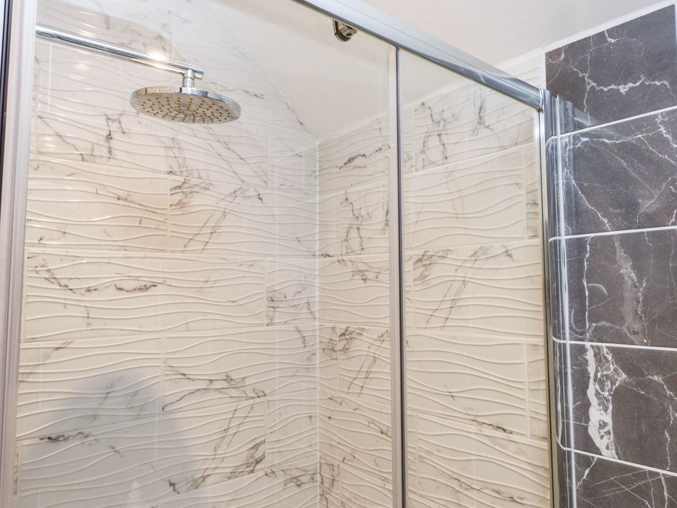 A shower with glass door and tiled walls at Tyddyn Elidir near Old Colwyn